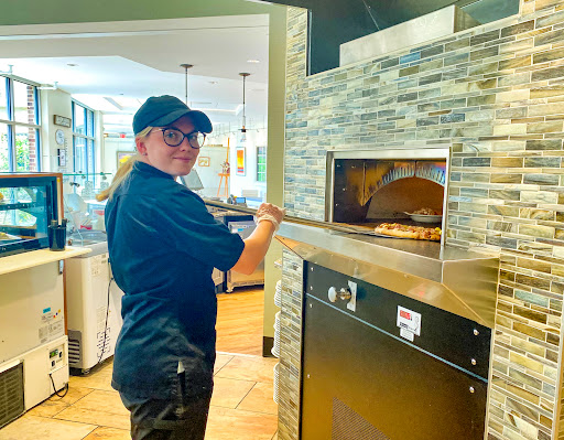 A chef carefully placing a pizza into the oven in a modern restaurant kitchen.