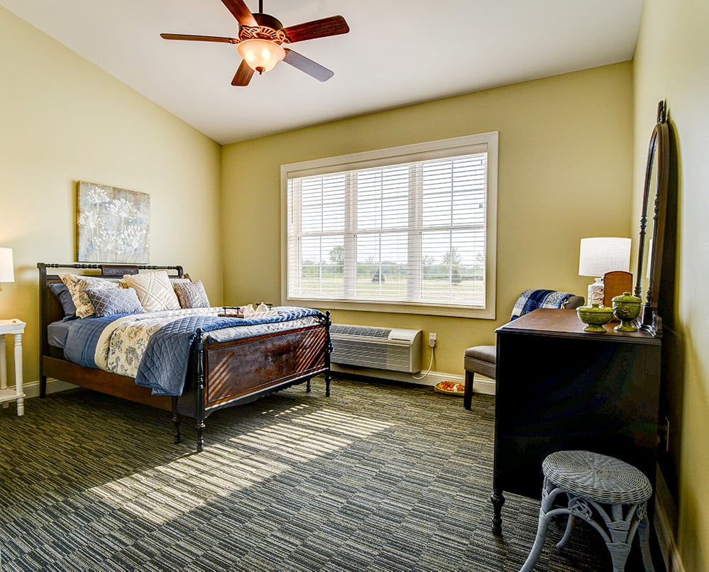 A cozy bedroom with a comfortable bed, a desk, and large window letting in natural light.
