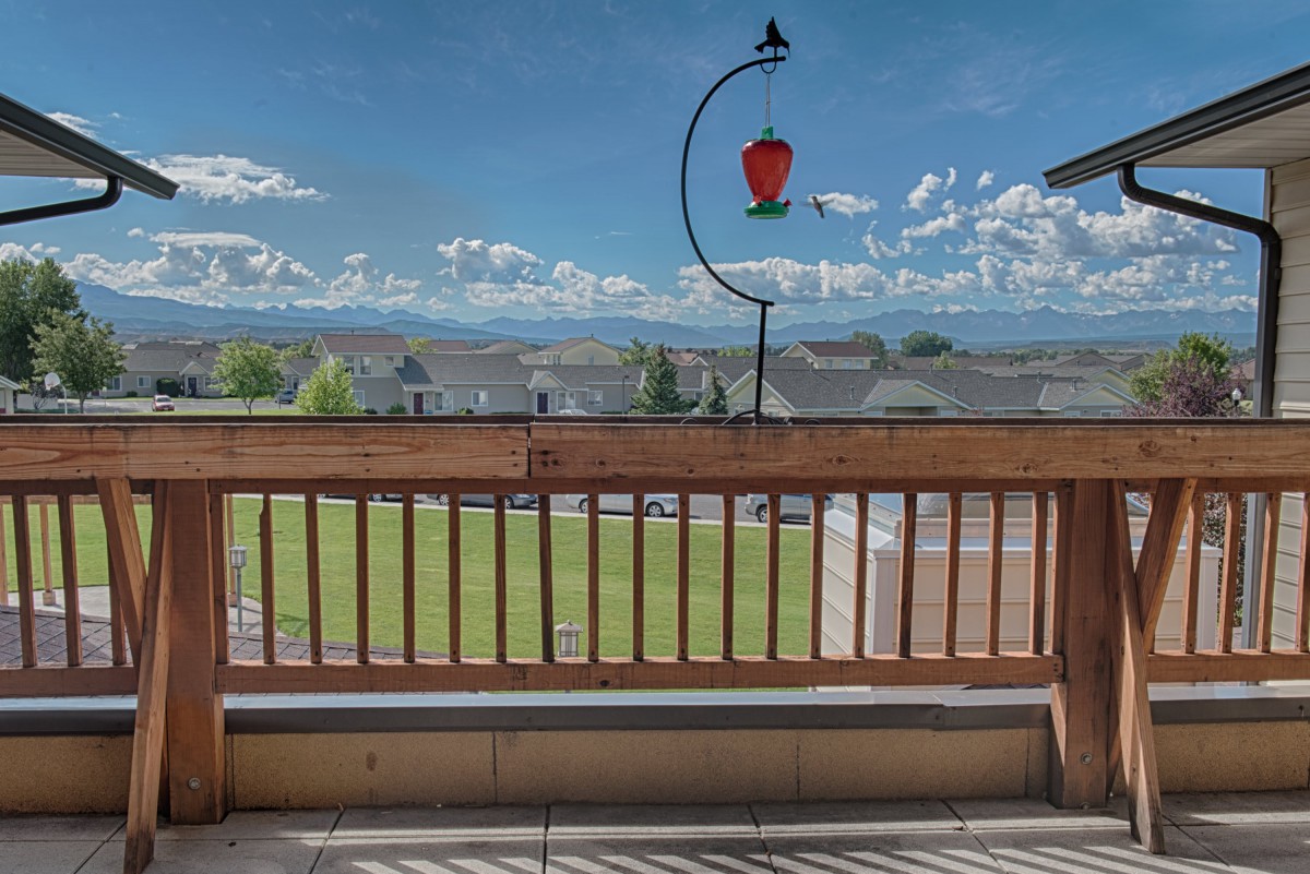 A scenic view from a balcony featuring mountains in the distance and a bird feeder hanging above a wooden railing.