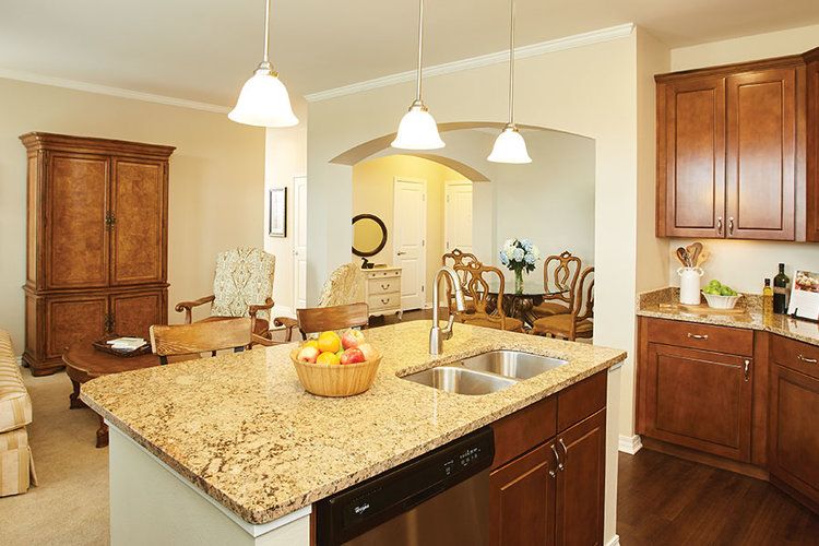 A modern kitchen featuring an island with a granite countertop, sink, and pendant lighting, adjacent to an open dining area.