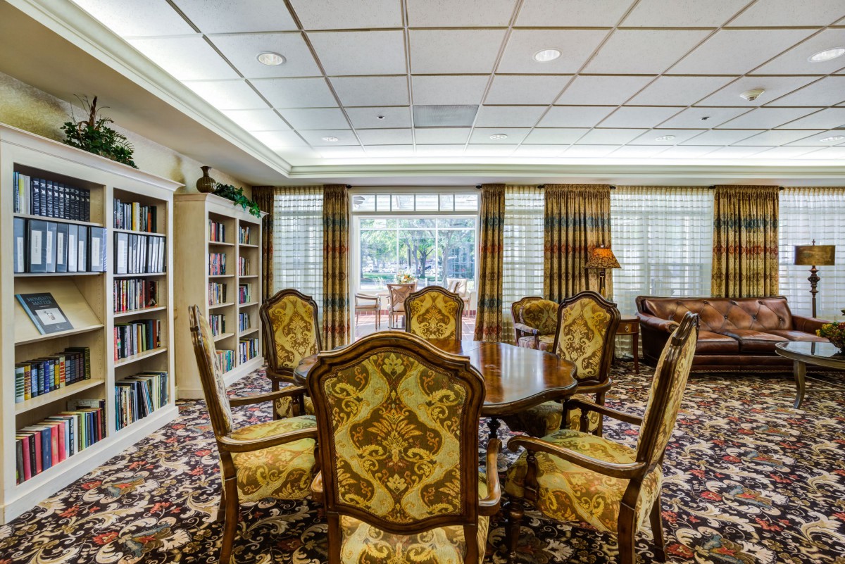 A cozy library room featuring ornate chairs, bookshelves, and large windows with elegant curtains.