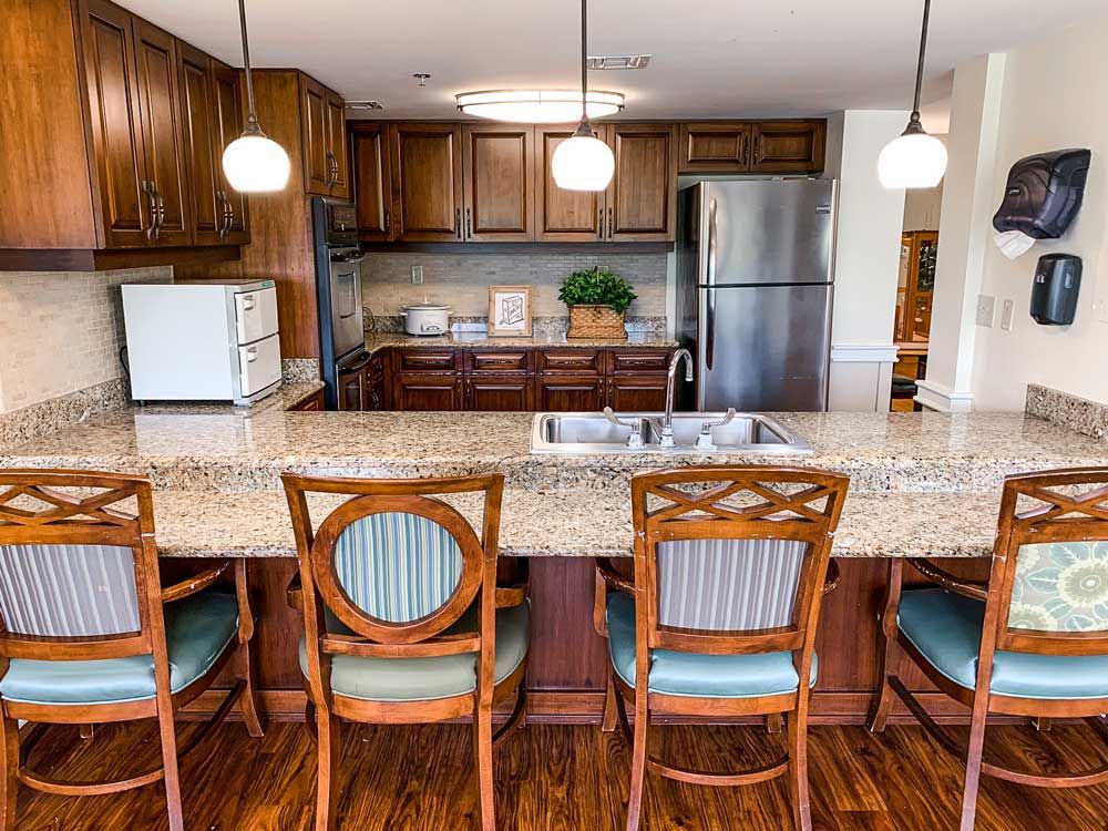 A cozy kitchen with wooden cabinetry and a granite countertop, featuring pendant lighting and comfortable seating.