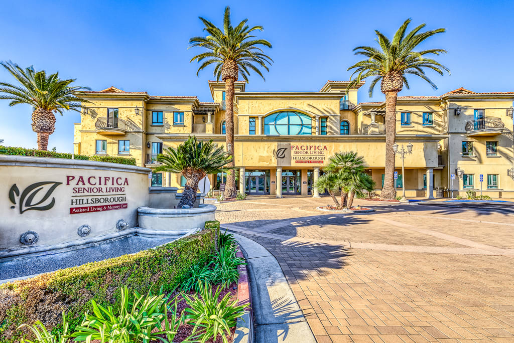 A luxurious hotel entrance featuring palm trees and a decorative fountain.