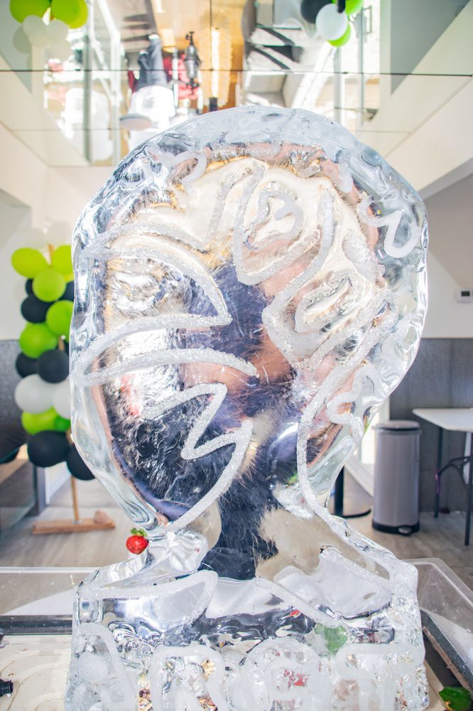 An ice sculpture displayed indoors, surrounded by decorative balloons.