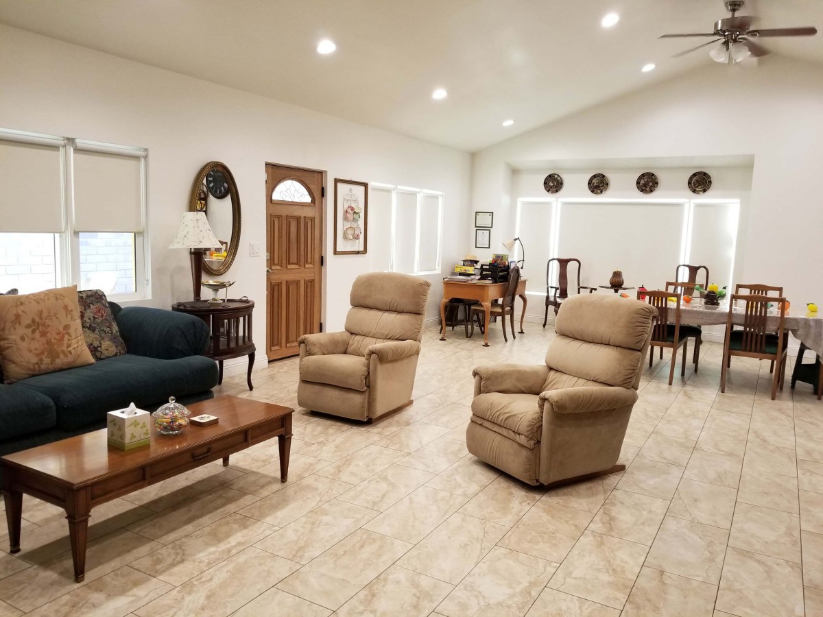A spacious living room with beige recliners, a dark sofa, and a dining area in the background.