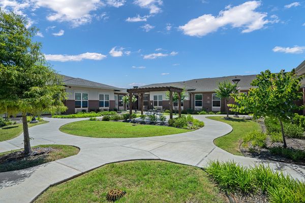 A beautifully landscaped garden with a pergola and pathways in front of modern buildings.