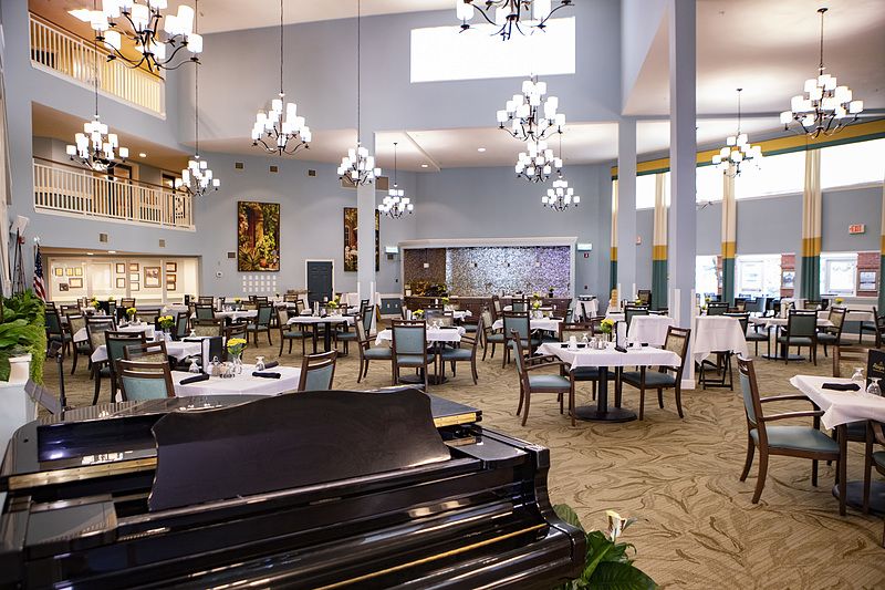 A spacious and elegant dining area with a piano, chandeliers, and well-arranged tables and chairs.