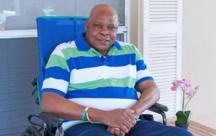 A man sitting indoors wearing a striped shirt.