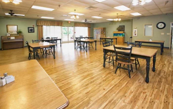A spacious room with wooden flooring, tables, and chairs arranged neatly.