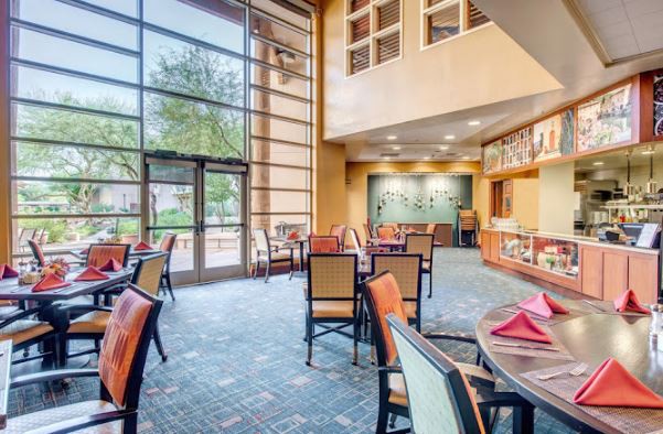A modern dining area with large windows allowing natural light to illuminate the space, featuring neatly arranged tables and chairs.
