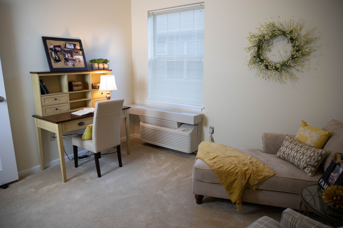 A cozy home office with a desk, chair, and sofa, featuring warm decor and soft lighting.