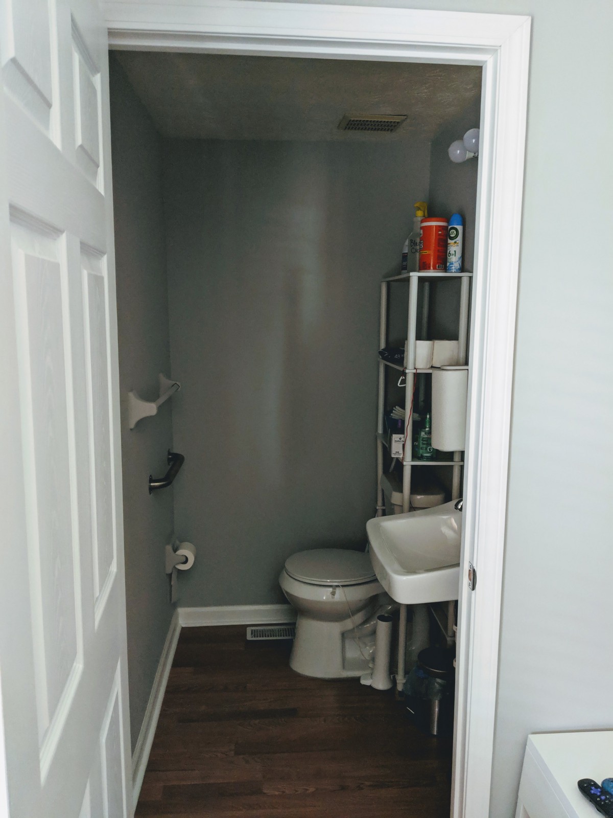 A small, minimalist bathroom with a toilet, sink, and metal shelving unit.