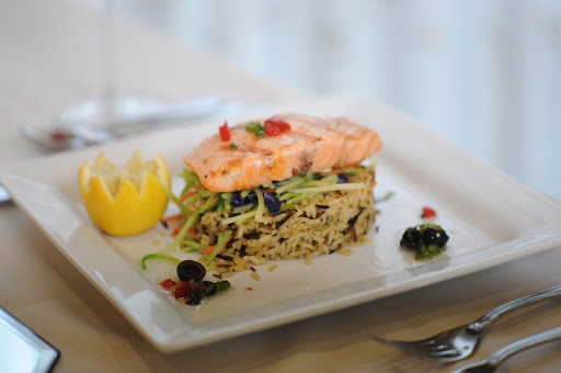 A delicious salmon dish served over a bed of seasoned rice, garnished with fresh ingredients.