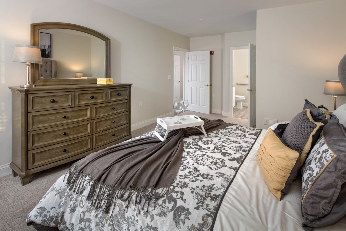 A cozy bedroom with a well-decorated bed, a wooden dresser with a mirror, and neutral color tones.