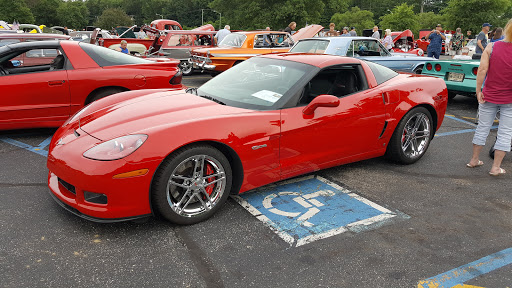A red Corvette parked over a handicap parking spot at a car show.