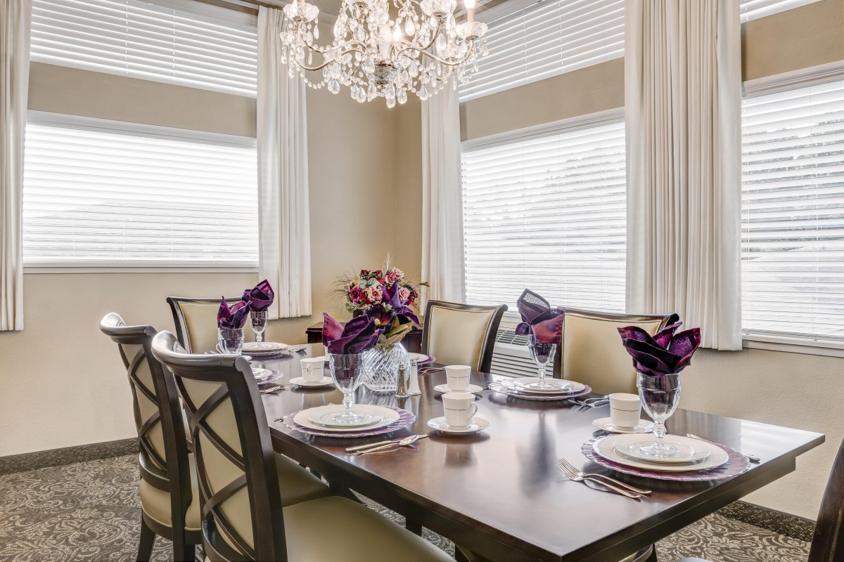 An elegantly set dining table with a chandelier hanging above, featuring purple napkins and tasteful decor.