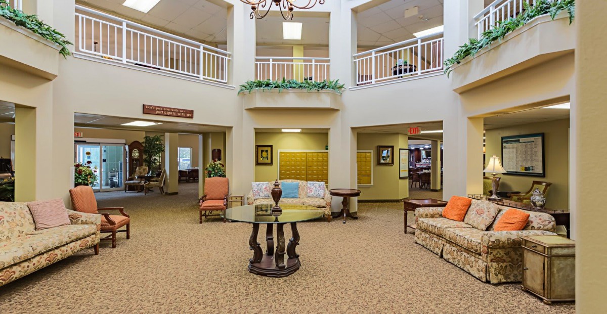 A spacious lobby area featuring sofas, a central round table, and a chandelier above.