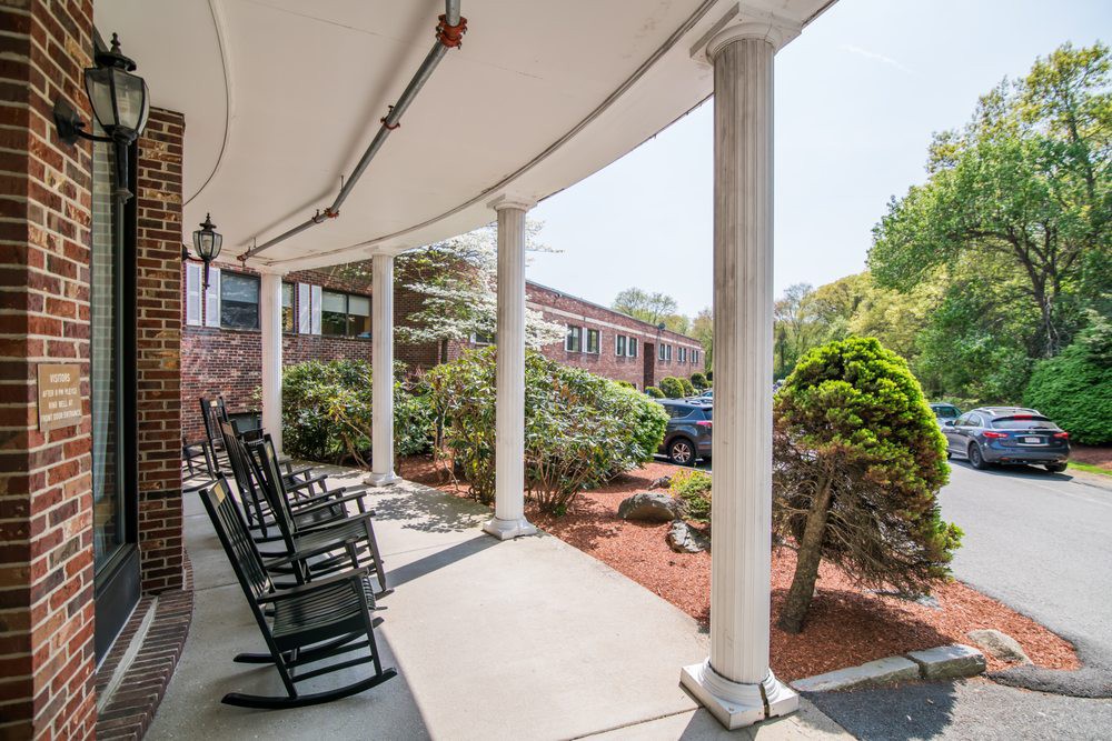 A sunny porch with columns and rocking chairs, surrounded by well-kept landscaping.