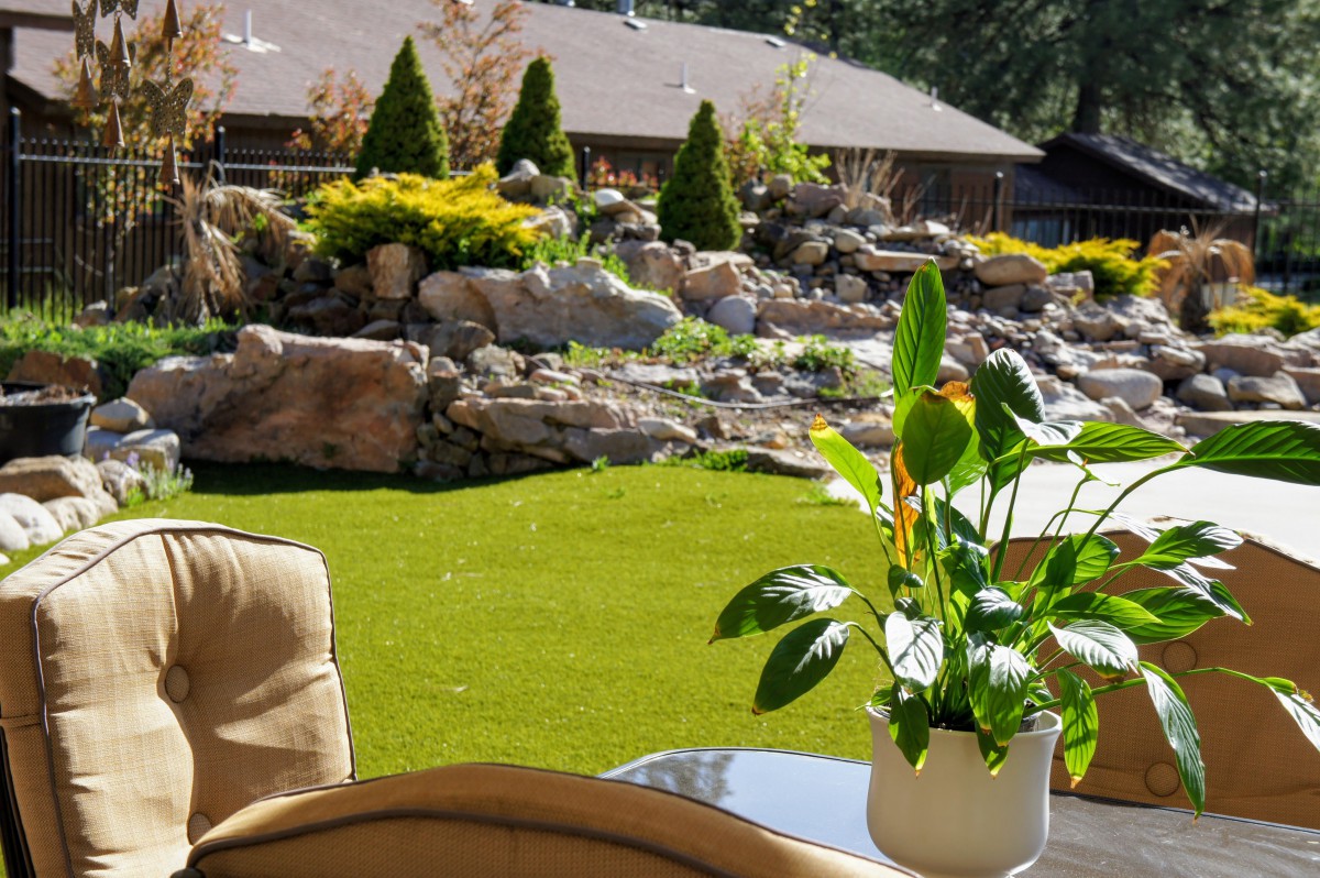 A peaceful backyard with lush greenery, a rock garden, and patio furniture.