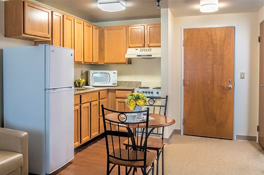 A cozy kitchen and dining area featuring wood cabinets, a refrigerator, microwave, electric stove, and a small table with chairs.