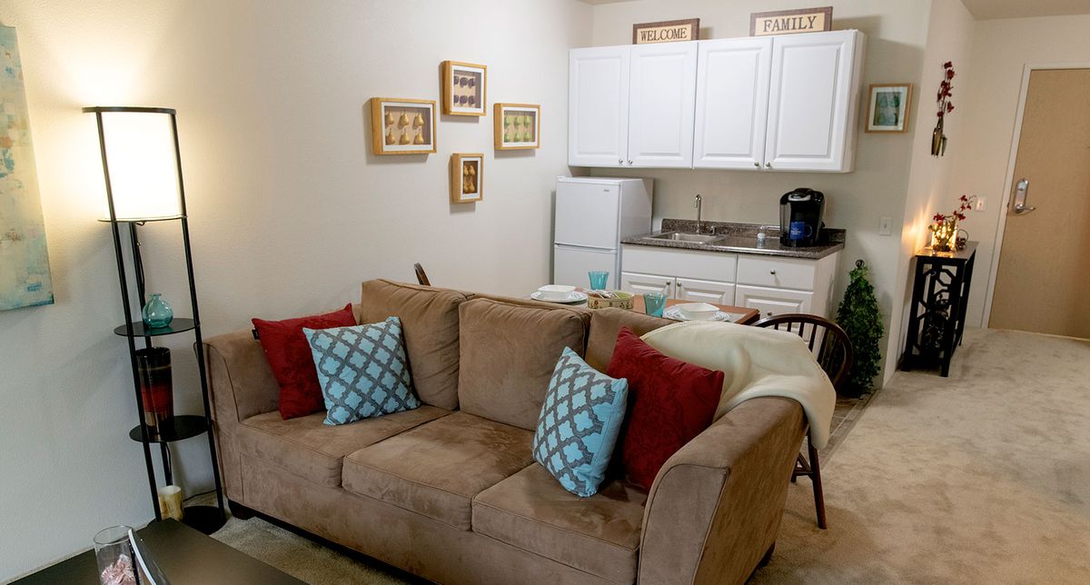 A cozy apartment living area with a sofa and a small kitchen in the background.