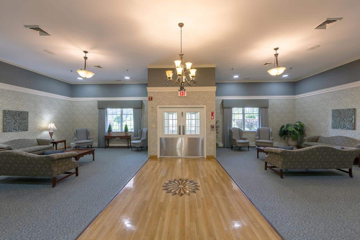 A spacious lobby area with a wooden floor, decorative chandelier, and comfortable seating.