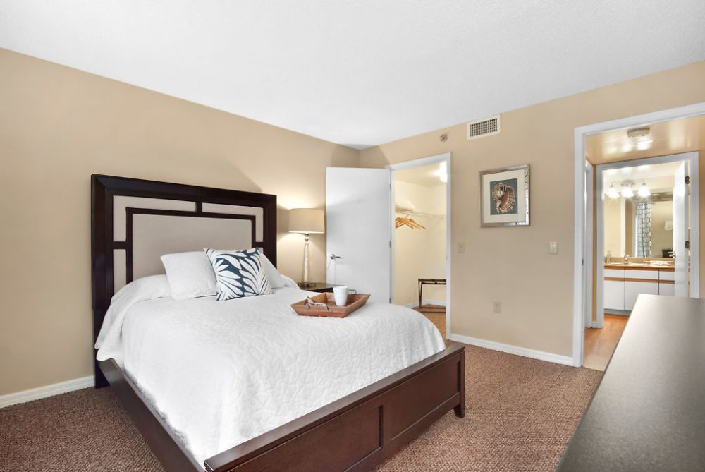 A cozy and minimalist bedroom featuring a large bed with decorative pillows and a bedside lamp.