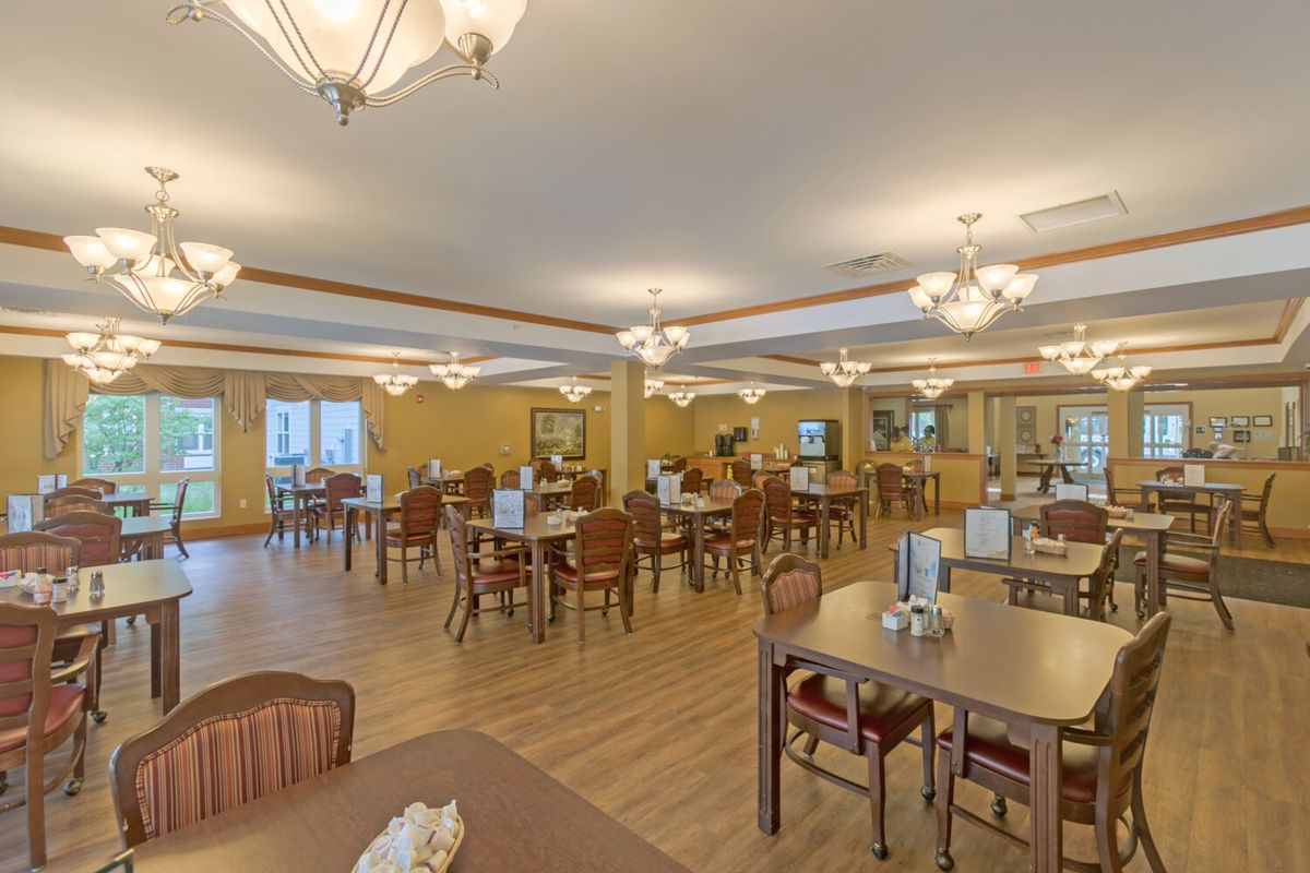 A spacious dining area with multiple tables and chairs, featuring warm lighting and wooden flooring.