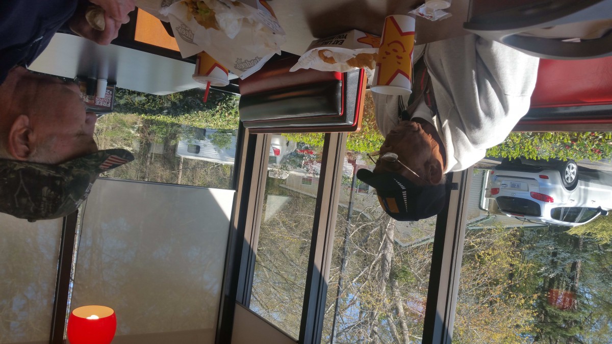 A person sitting at a table in a restaurant with food on the table, next to a window.