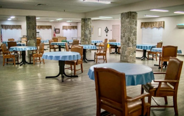 An empty dining area with tables covered in blue tablecloths and wooden chairs.