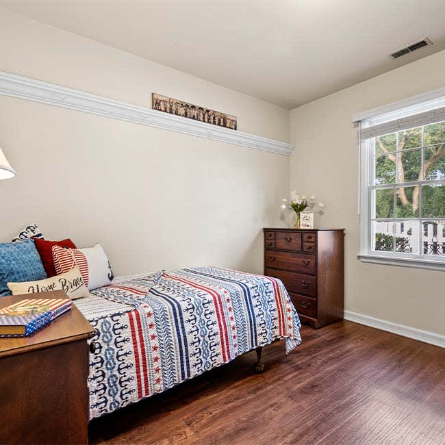 A cozy bedroom with a single bed, colorful bedding, and a window allowing natural light.