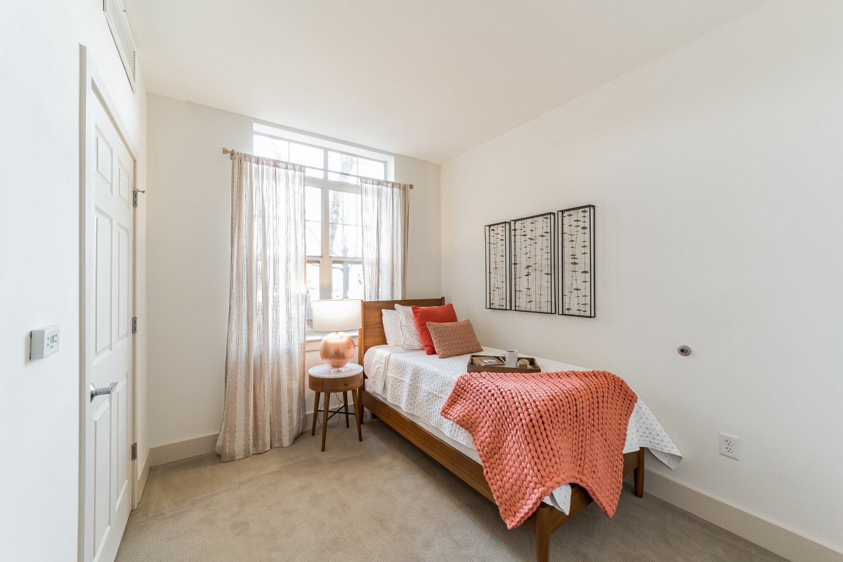 A cozy minimalist bedroom with a single bed, bright natural light, and simple decor.