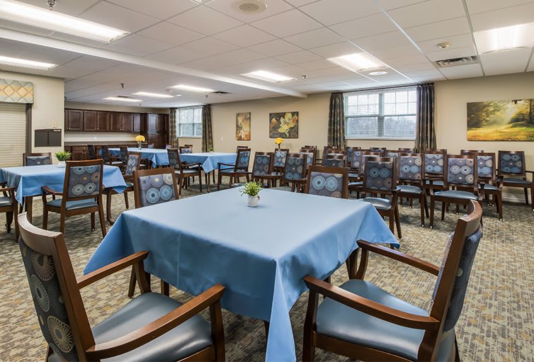 A spacious dining room with neatly arranged tables and chairs, featuring blue tablecloths and simple decor.