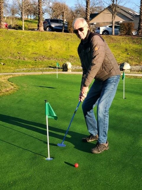 Person enjoying a game of mini-golf on a sunny day.
