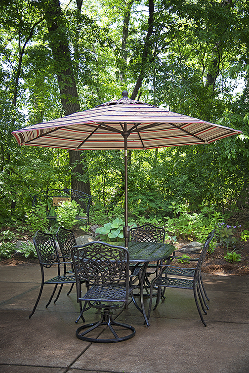 A scenic outdoor patio area featuring a table with chairs and a large umbrella, surrounded by lush greenery.