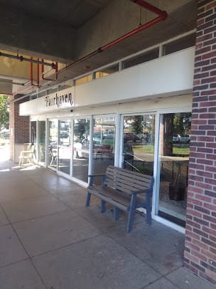 Exterior view of a restaurant with glass windows and a wooden bench outside.