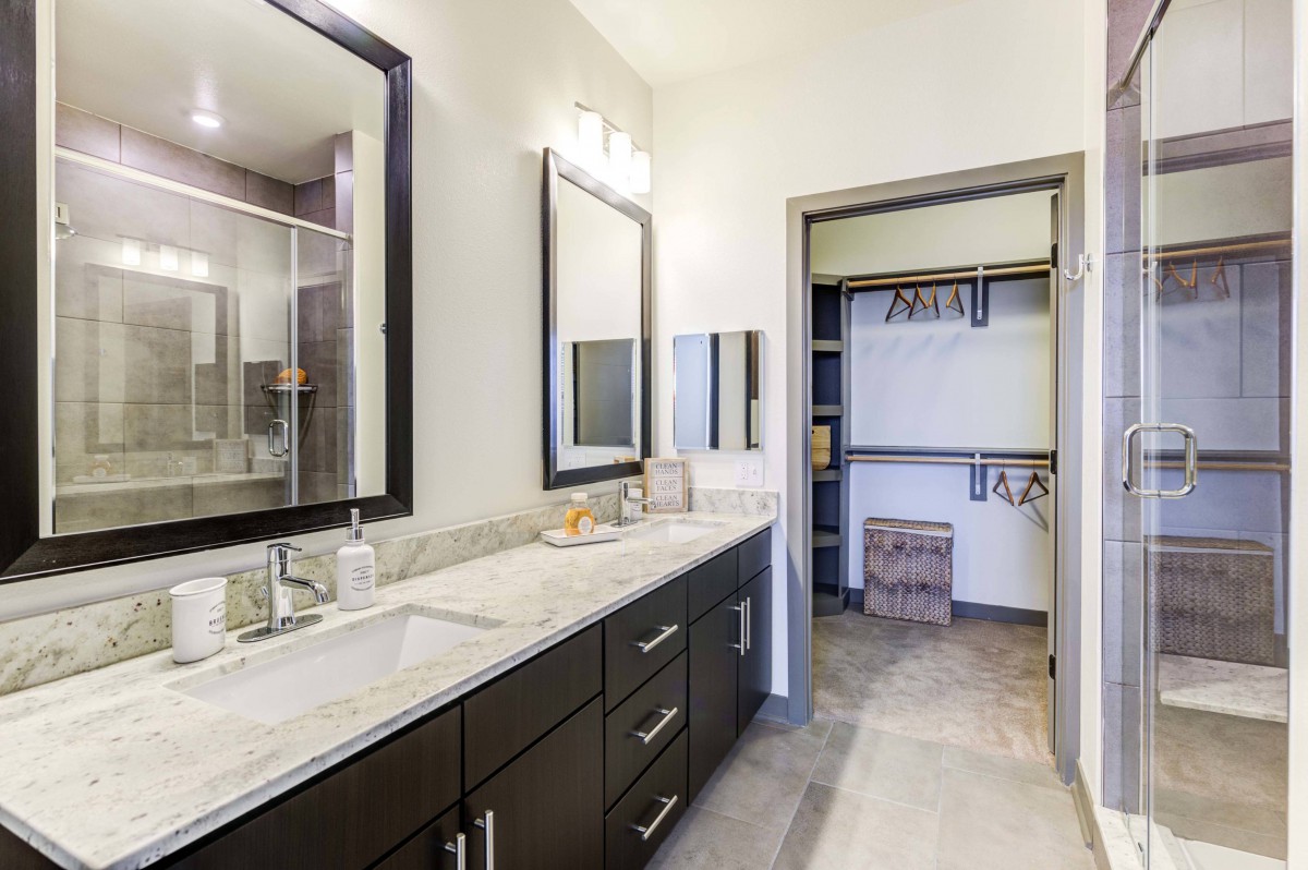 A modern bathroom with dual sinks and a walk-in closet.