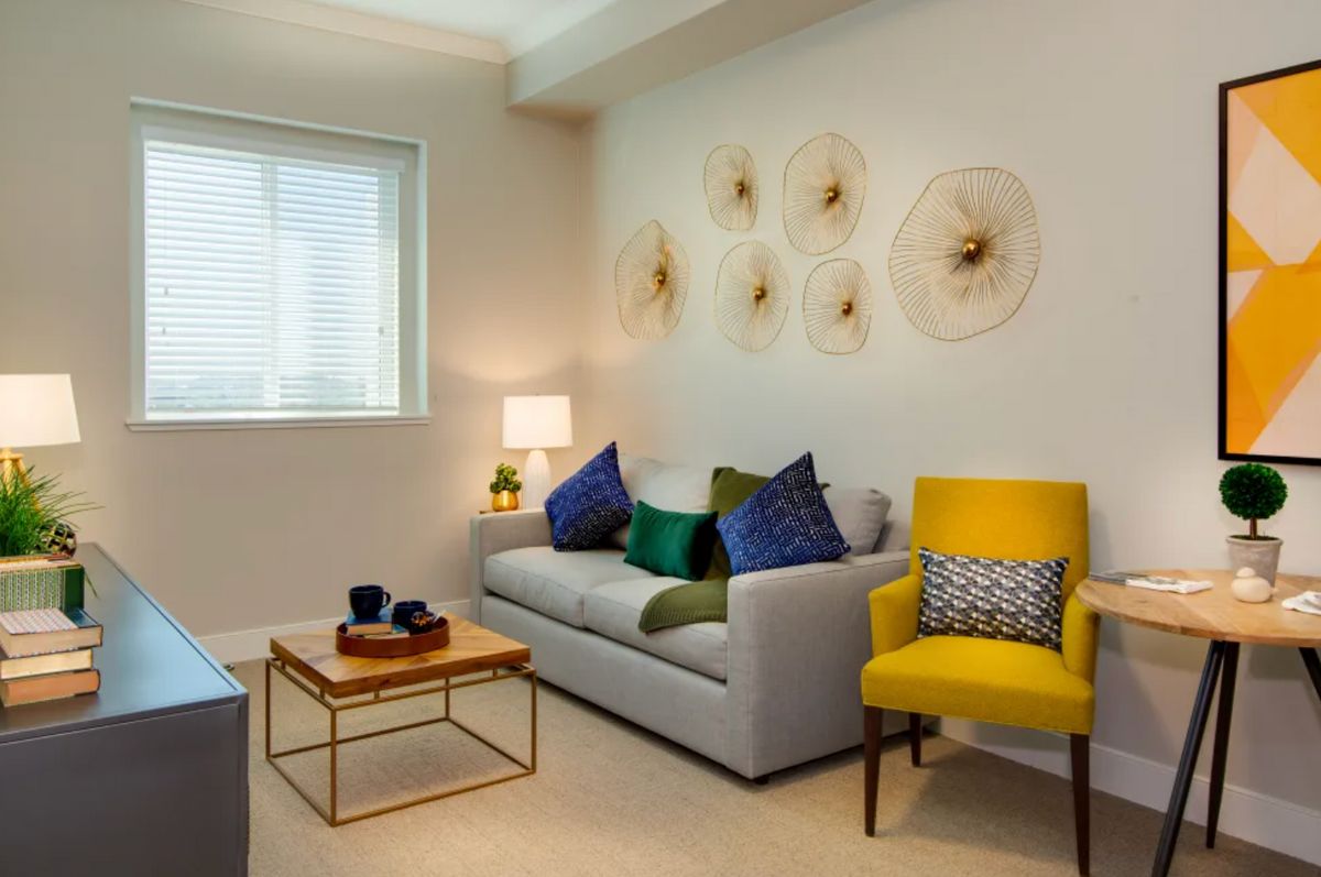 A modern living room with a stylish couch, colorful pillows, and a yellow chair.