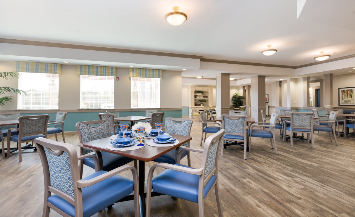 A well-lit dining area featuring blue-upholstered chairs and wooden tables on a wood floor.