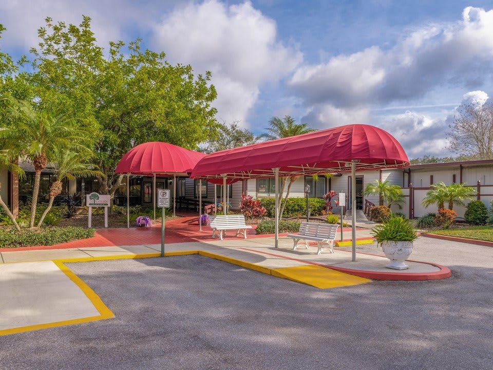 Building entrance with a red canopy and landscaped surroundings on a cloudy day.
