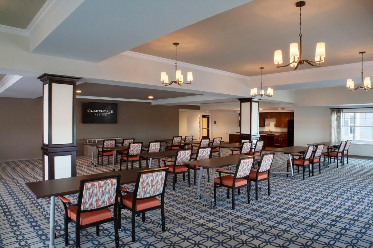 A spacious conference room with rows of chairs and tables, equipped with a projector screen.
