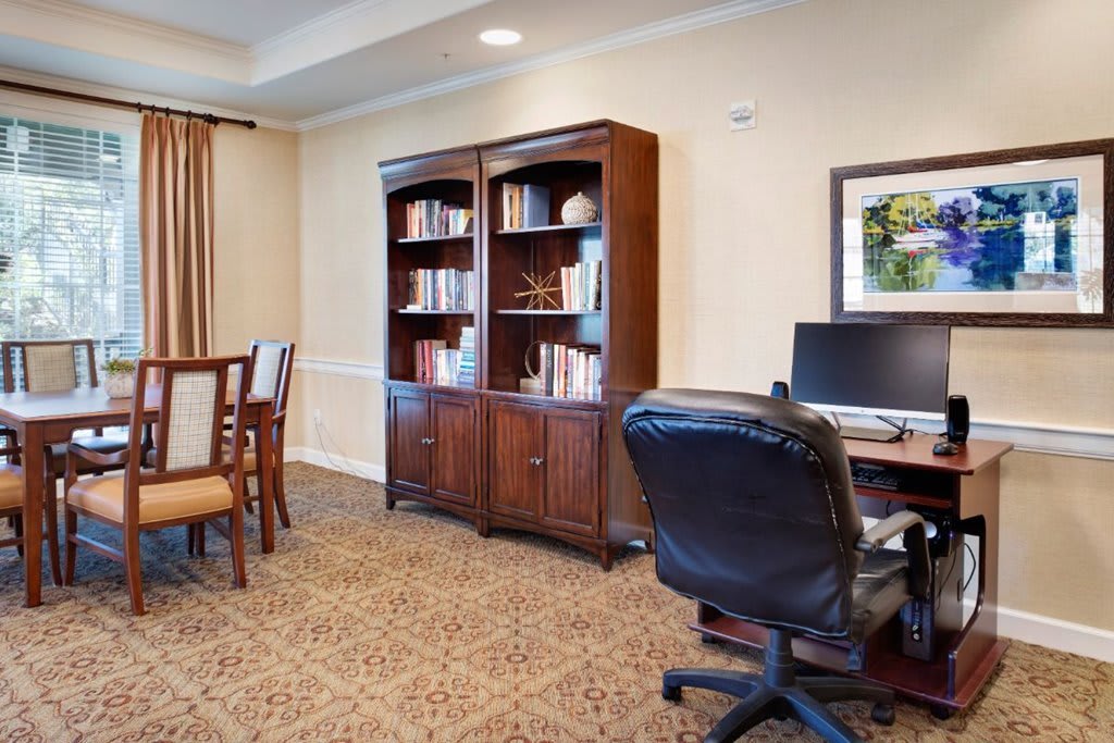 A well-organized office space featuring a desk with a computer, a comfortable chair, and a large wooden bookshelf filled with books.