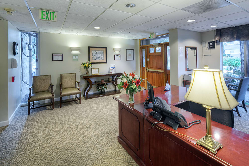 A well-appointed office reception area with a wooden desk, chairs, and decorative elements like flowers and framed pictures.