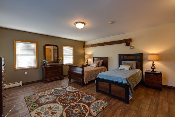 A cozy bedroom featuring two beds, wooden furniture, and a decorative rug.