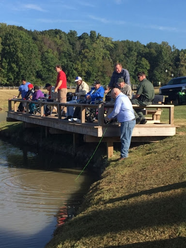 A group of people enjoying a day of fishing off a wooden pier by the lake.