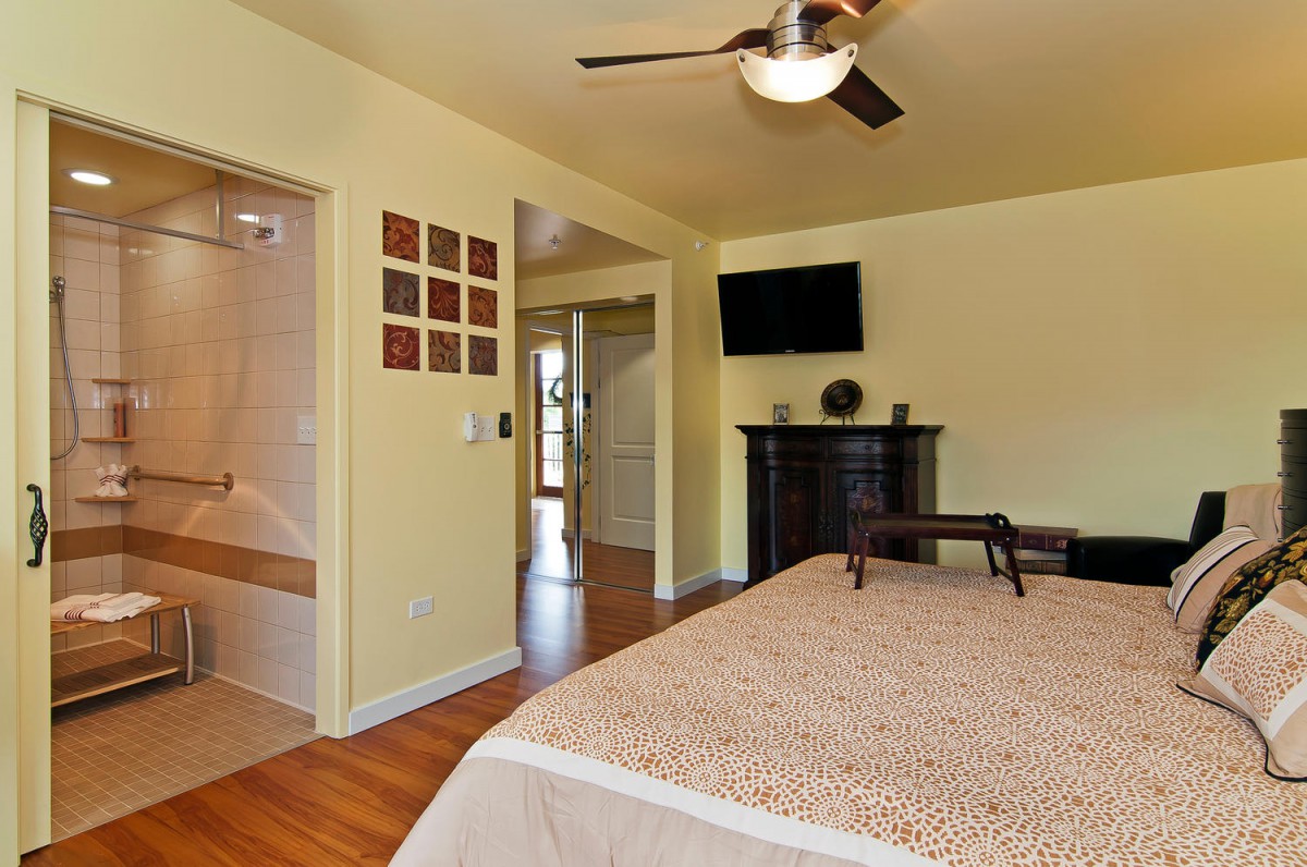 A cozy bedroom with a ceiling fan and a wall-mounted television.