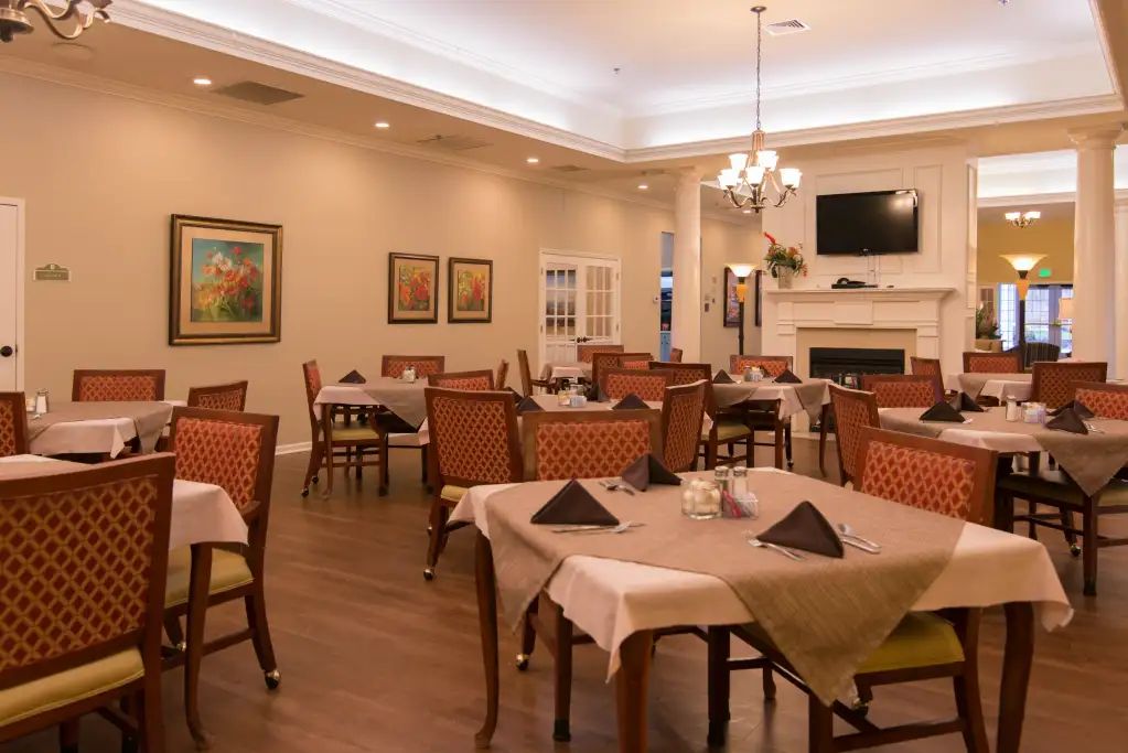 A cozy and elegant dining area with neatly arranged tables and chairs, featuring a fireplace and chandelier.