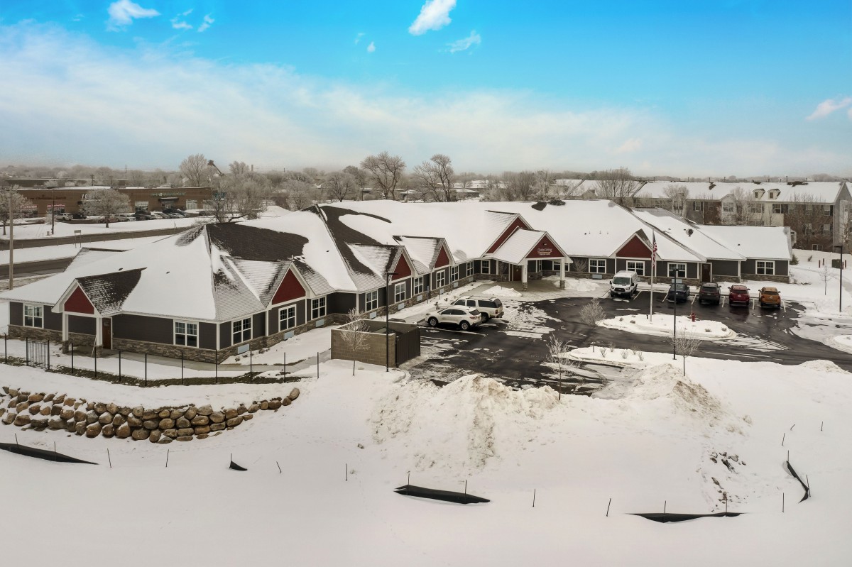 A snowy landscape with a series of buildings and a parking lot under a clear blue sky.