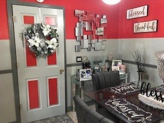 A cozy dining area with red and gray decor, featuring a wreath on the door and framed pictures.