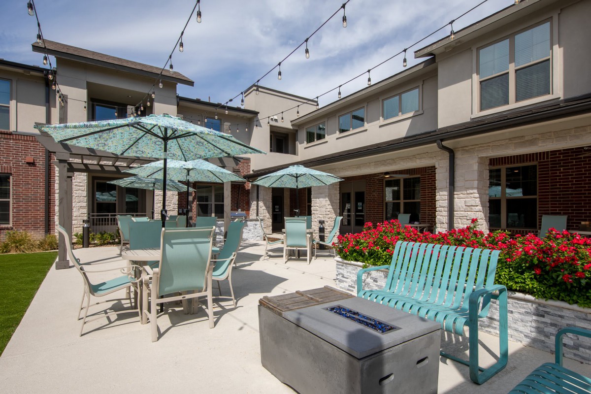 A sunny outdoor patio with seating and umbrellas, surrounded by a modern building.